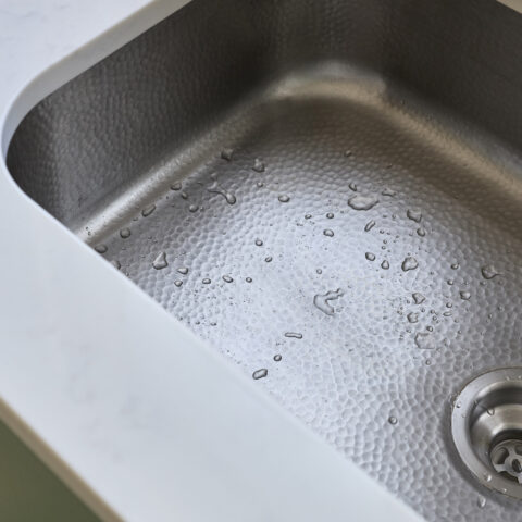 A stainless rectangular undermount sink with stainless drain and water beads in basin
