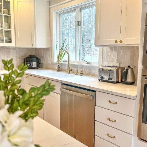 White kitchen with a window over the fireclay sink and stainless appliances.