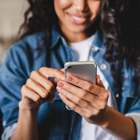 Smiling african american woman using smartphone at home, shopping online, while relaxing on couch