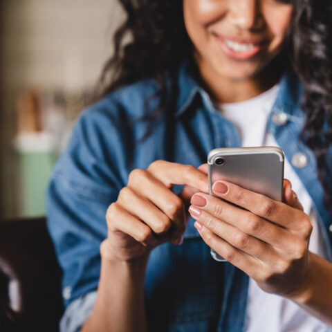 Smiling african american woman using smartphone at home, shopping online, while relaxing on couch