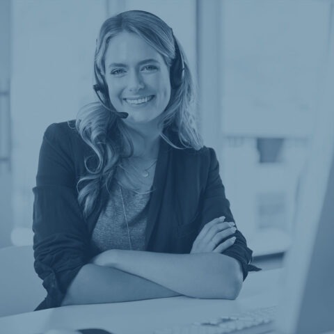 Colorized photo of smiling female customer service representative with phone headset on sitting at a desk with a computer