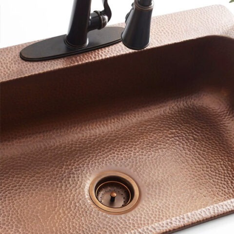 Copper drop-in kitchen sink with bronze faucet and drain in white countertop