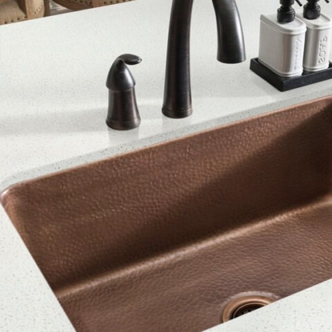 Undermount copper kitchen sink with dark faucet and light countertop