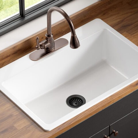 Drop-in fireclay kitchen sink with bronze faucet and drain set in a wood countertop with dark cabinets under a large window