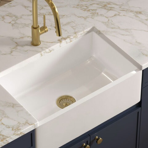 Fireclay farmhouse kitchen sink overhead view with marble countertop, blue cabinets and gold faucet and drain