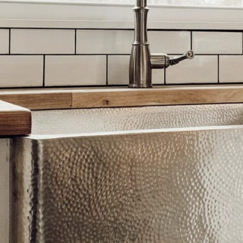 Stainless steel kitchen farmhouse sink with subway tile backsplash, butcher block countertop and under a large picture window